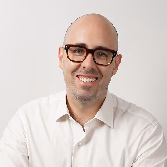 Bald man with glasses smiles in front of a white background