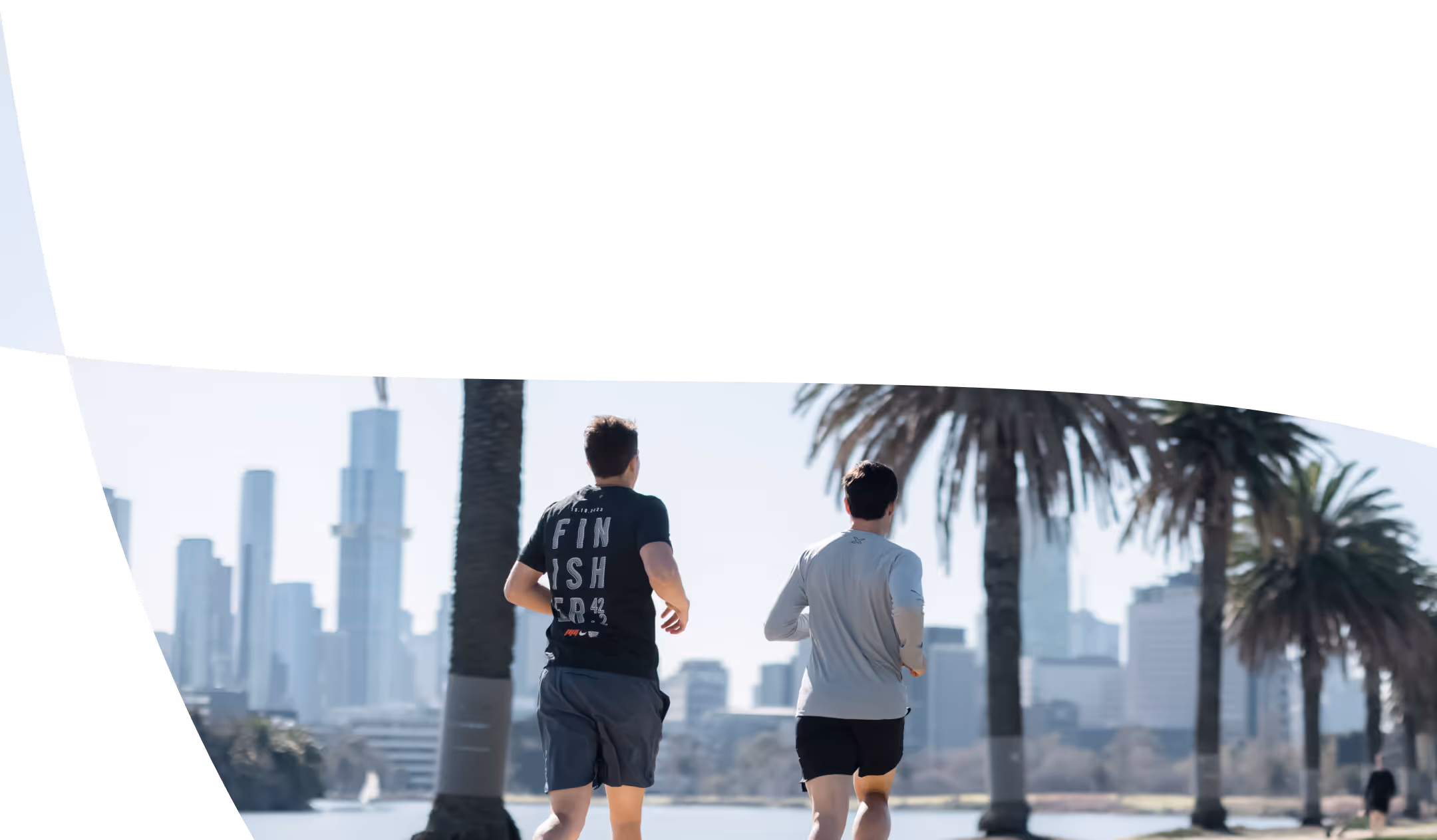 Two men run along a path with palm trees and city skyline