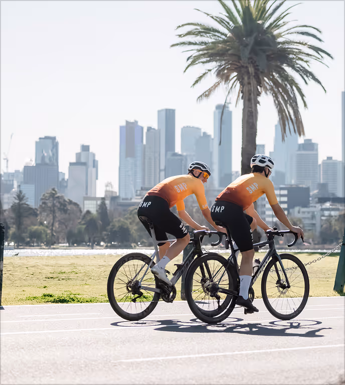 Two cyclists wearing SMP jerseys ride bikes on a path